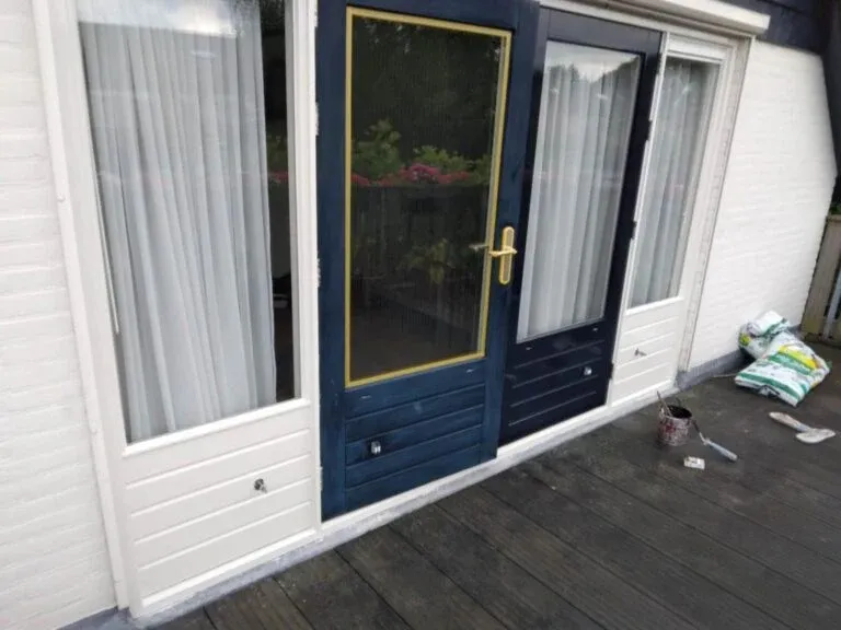 Donkerblauwe voordeur met witte kozijnen, afgeplakt tijdens schilderwerk